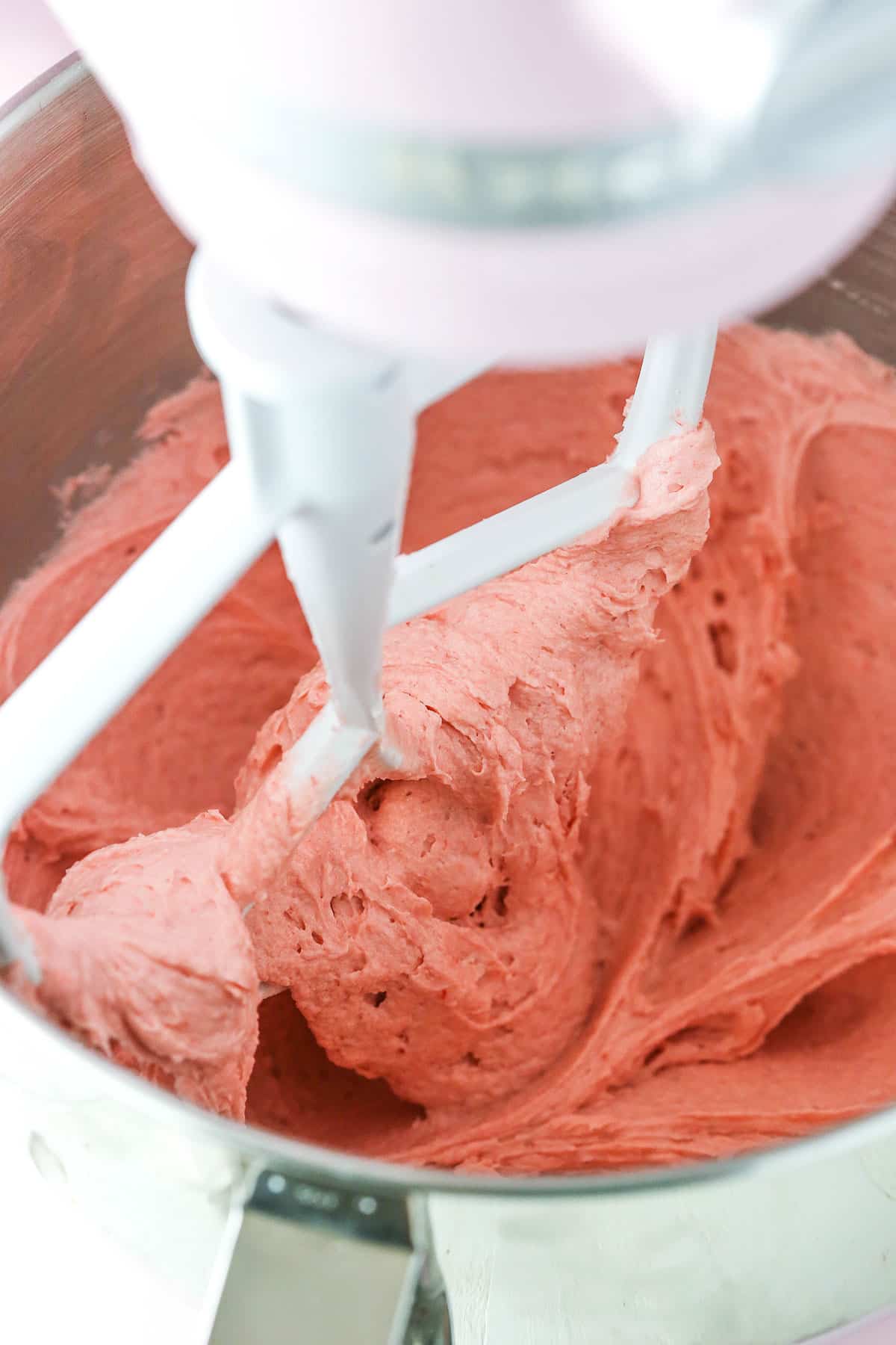 Homemade Strawberry Frosting being mixed using a mixer in a silver bowl