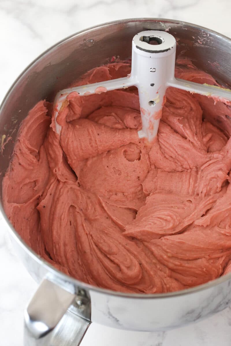 Adding strawberry puree, vanilla extract, strawberry extract, milk, and gel icing color to complete pound cake batter.