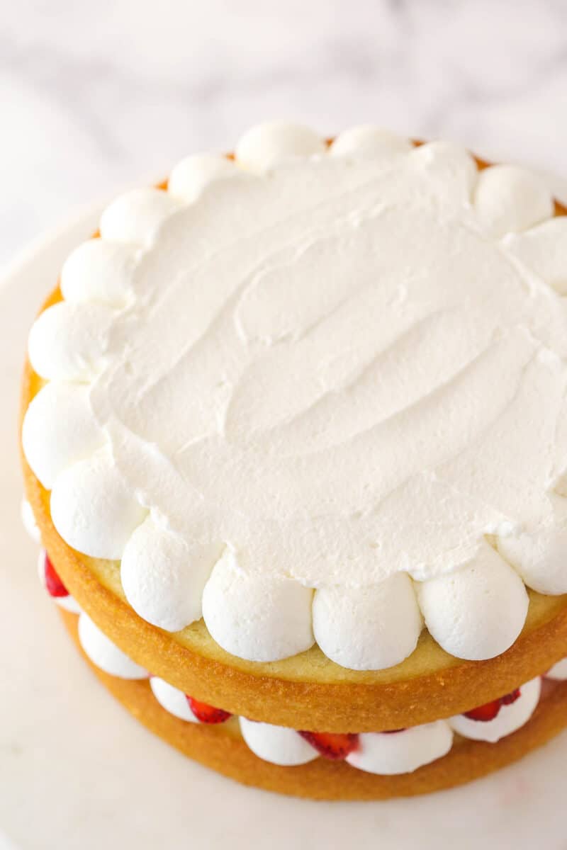 Topping strawberry shortcake cake with whipped cream.