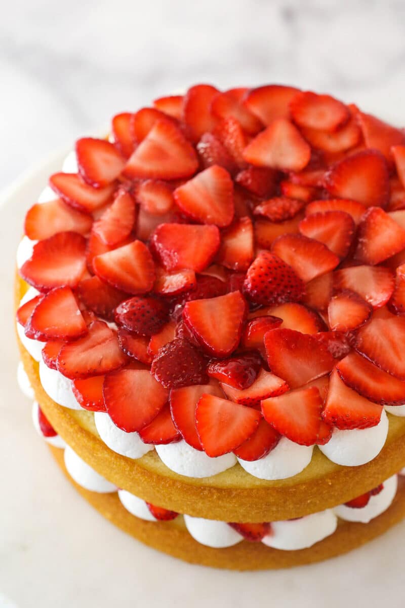 Adding strawberries to the second layer of strawberry shortcake cake.