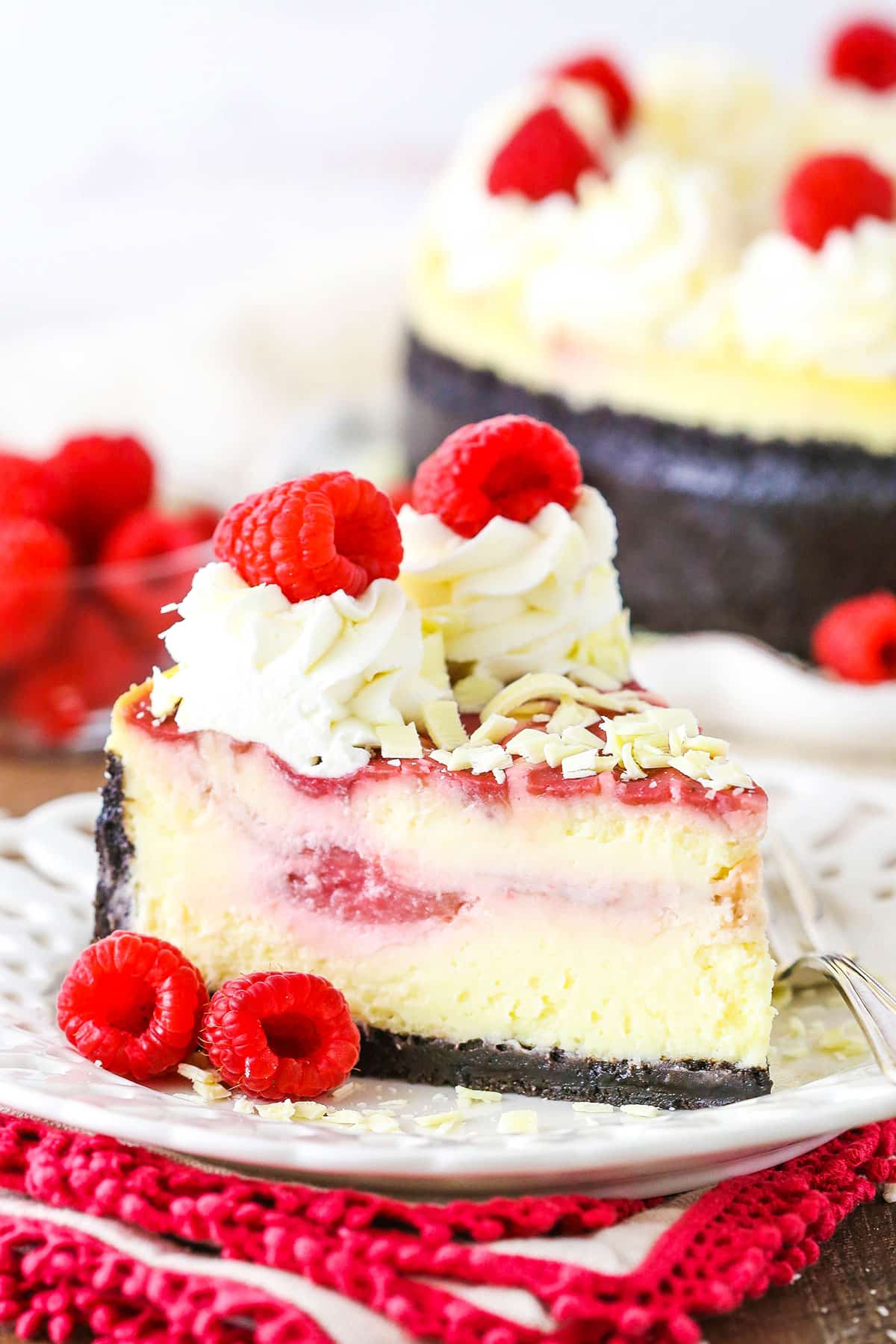 A slice of White Chocolate Raspberry Cheesecake next to a fork on a white plate