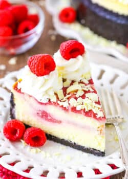 A slice of White Chocolate Raspberry Cheesecake next to a fork on a white plate