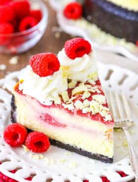 A slice of White Chocolate Raspberry Cheesecake next to a fork on a white plate