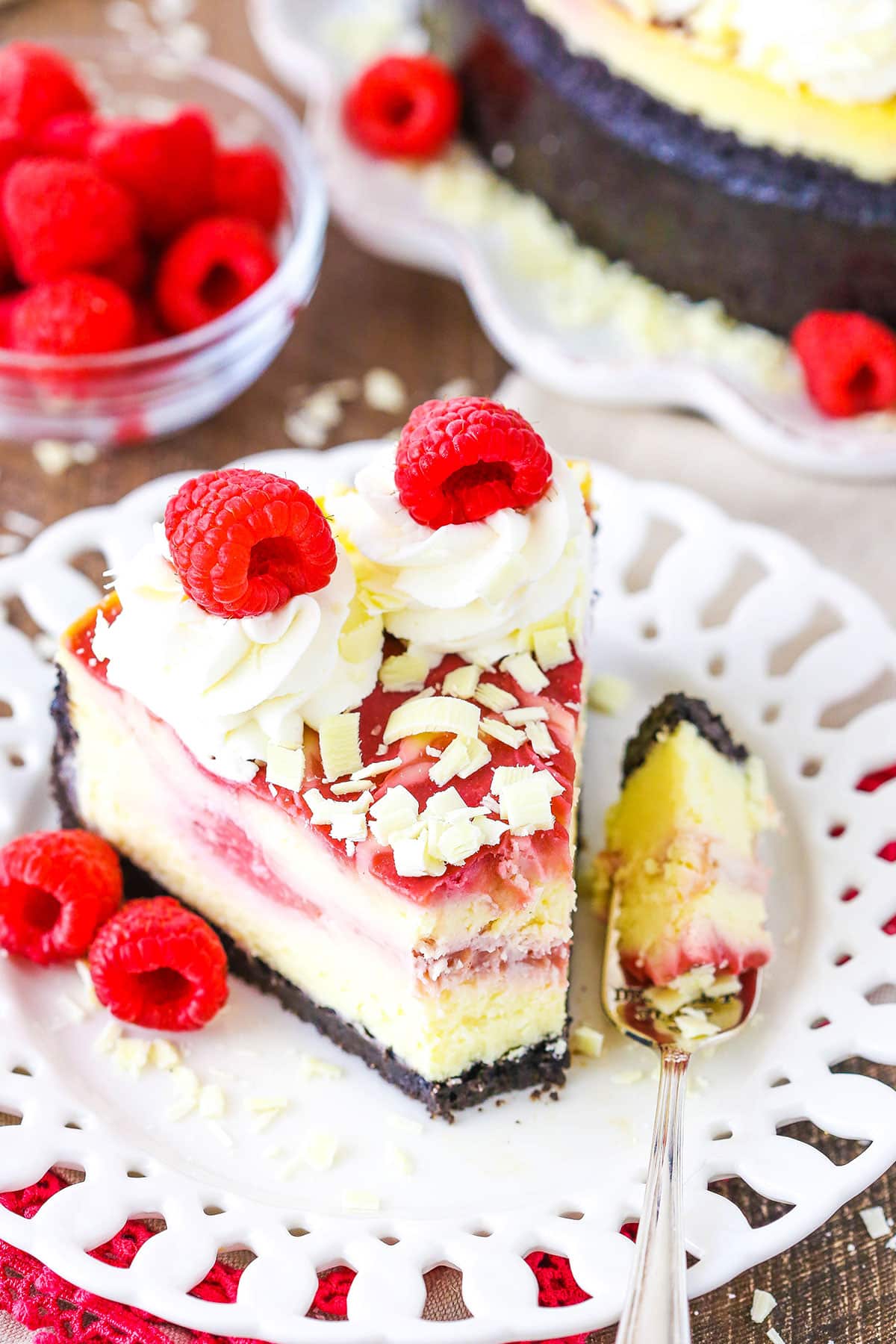 A slice of White Chocolate Raspberry Cheesecake with a bite removed next to a fork on a white plate