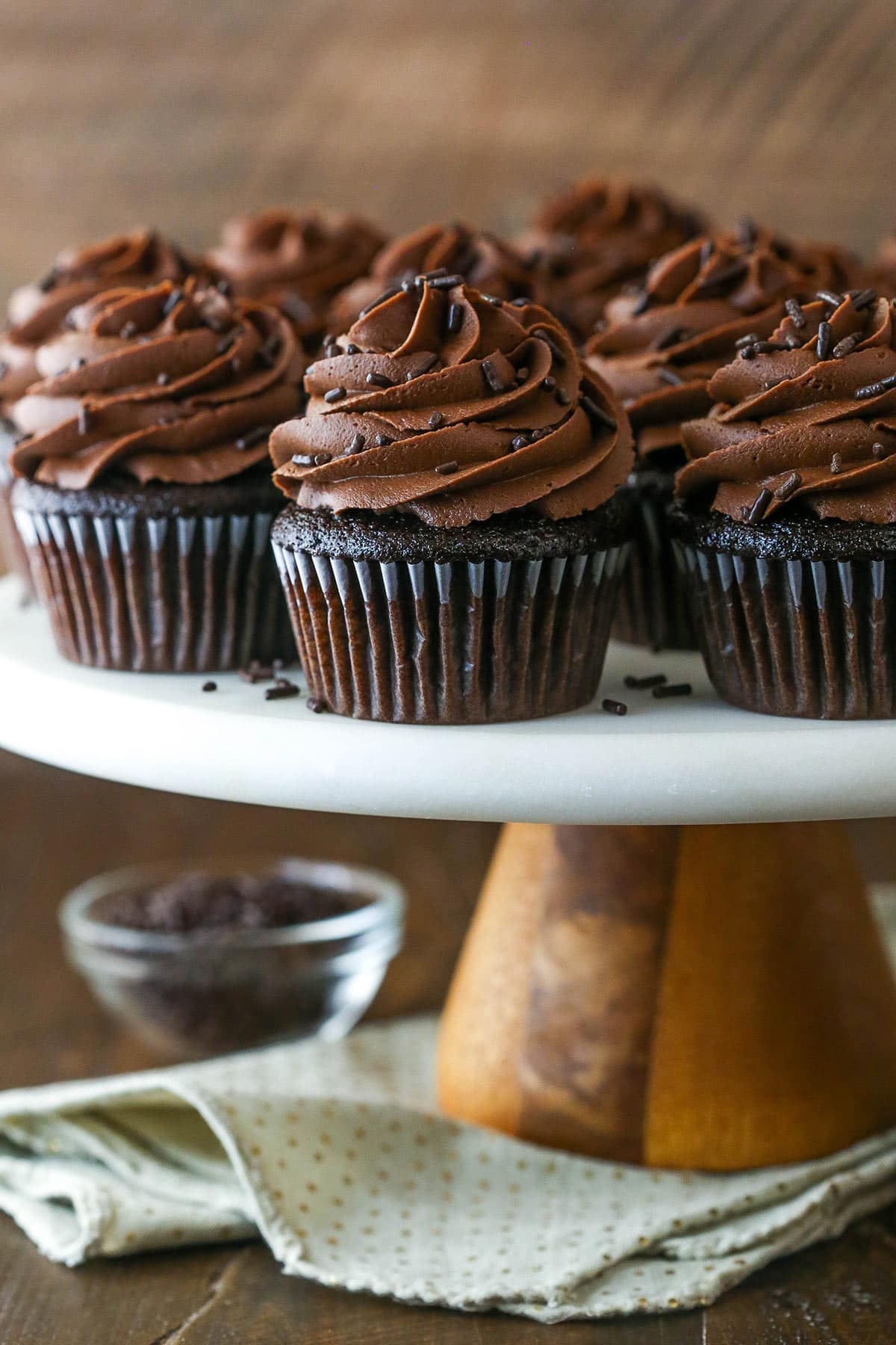 Moist chocolate cupcakes on a cake stand near a bowl of chocolate chips.