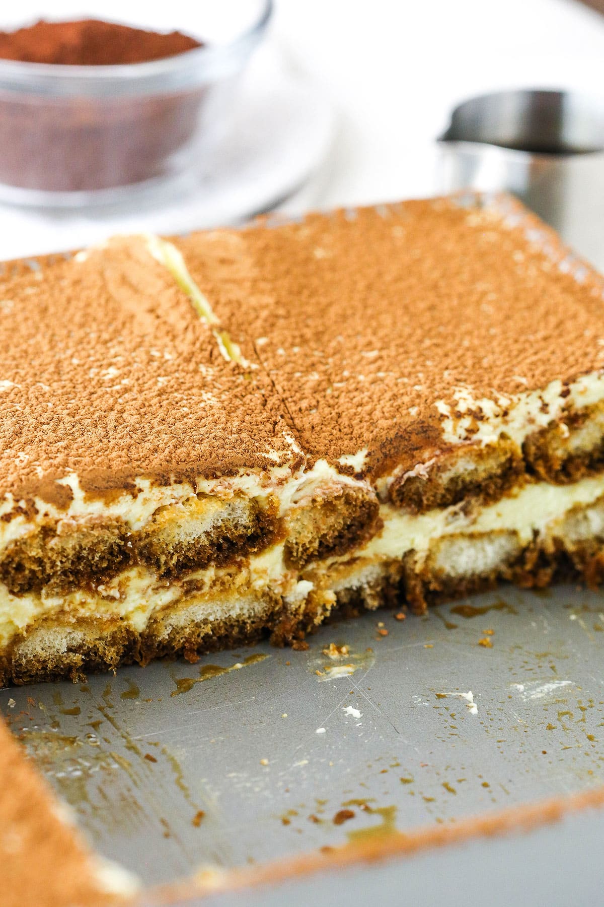 This easy tiramisu recipe is beyond decadent! Made with layers of espresso-soaked Ladyfinger cookies, fluffy mascarpone cream, and plenty of chocolate. Side view of a serving of Easy Tiramisu in a grey baking pan