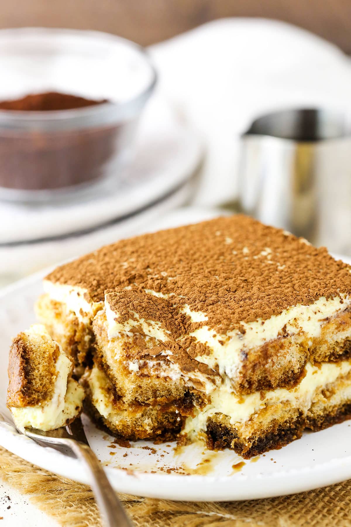 A square serving of Easy Tiramisu with a bite taken out next to a fork on a small white plate