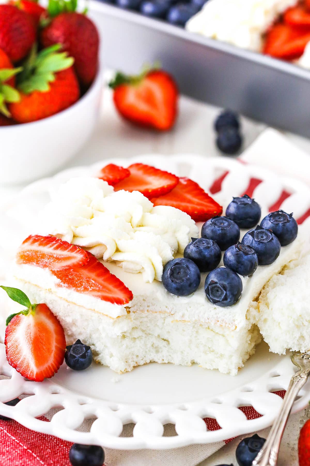 A serving of Angel Food Flag Cake with a bite removed next to a fork on a white plate