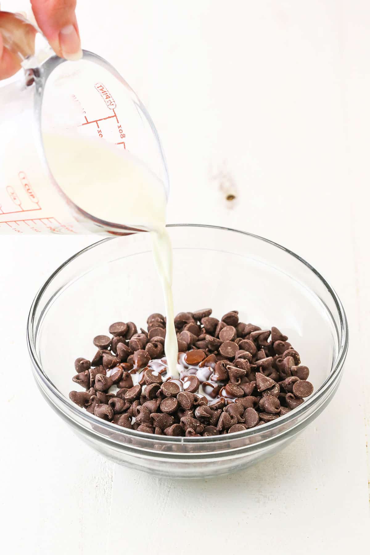Pouring the heavy whipping cream over chocolate chips in a glass bowl
