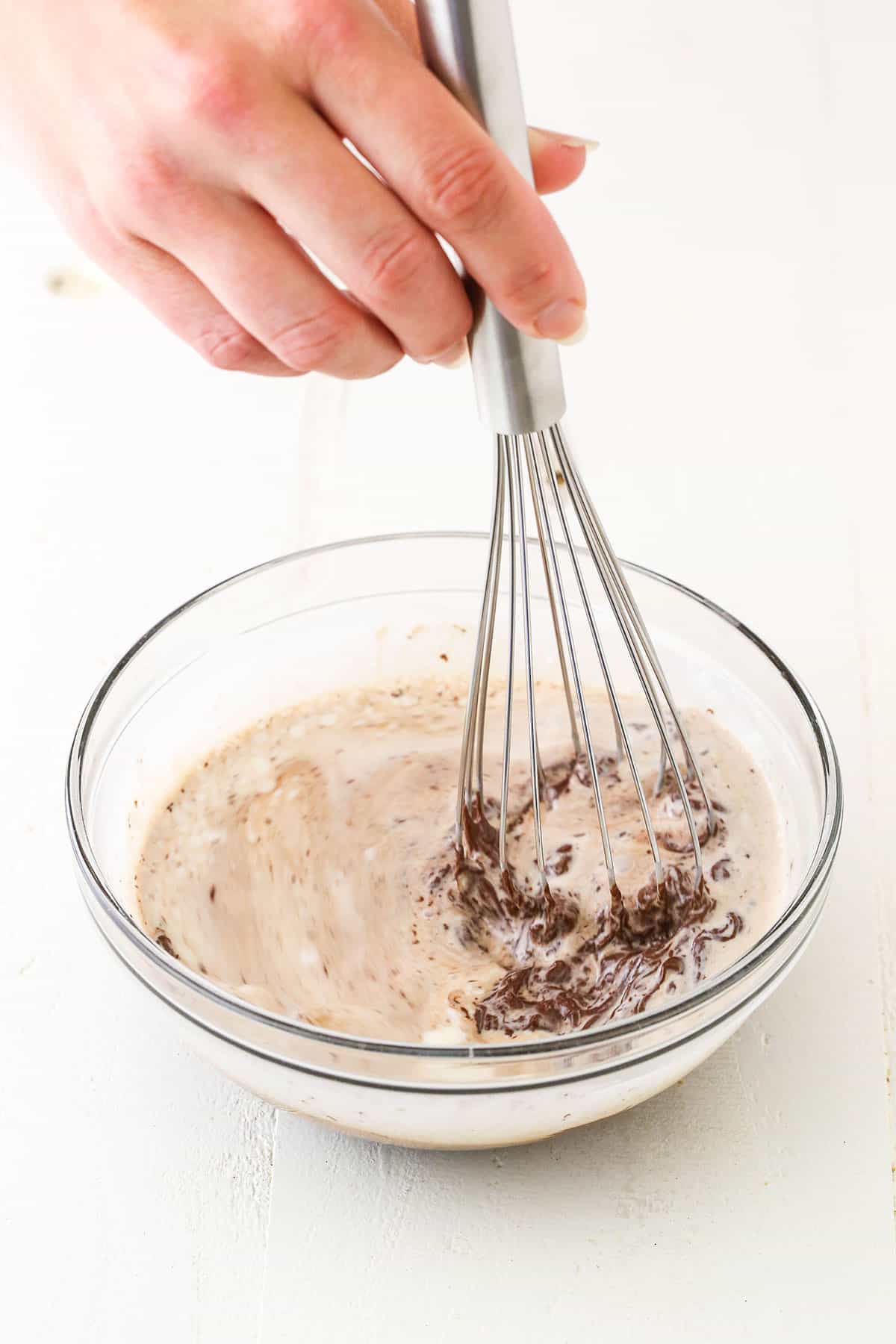 Whisking heavy whipping cream poured over chocolate chips in a glass bowl