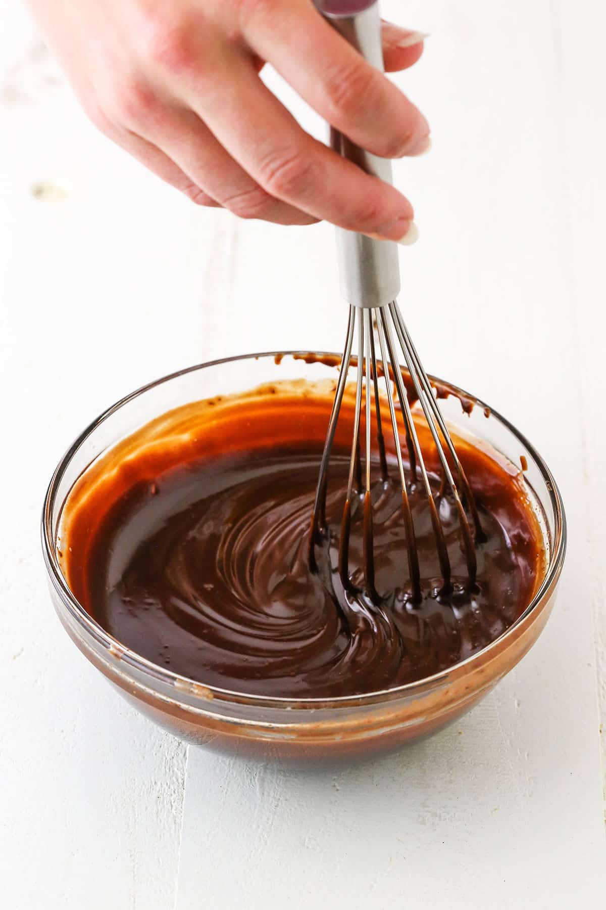 Mixing chocolate ganache using a whisk in a glass bowl