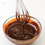 Dripping chocolate ganache off a whisk into a clear glass bowl