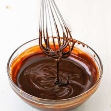 Dripping chocolate ganache off a whisk into a clear glass bowl