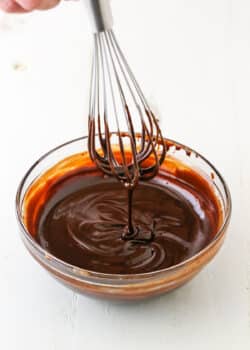 Dripping chocolate ganache off a whisk into a clear glass bowl