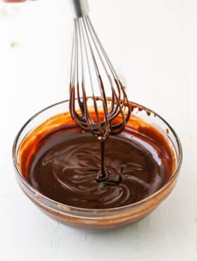 Dripping chocolate ganache off a whisk into a clear glass bowl