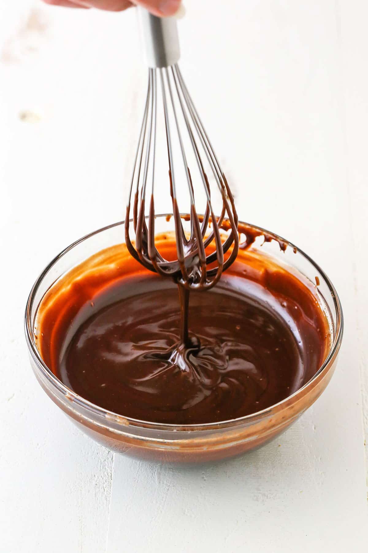 Dripping chocolate ganache off a whisk into a clear glass bowl