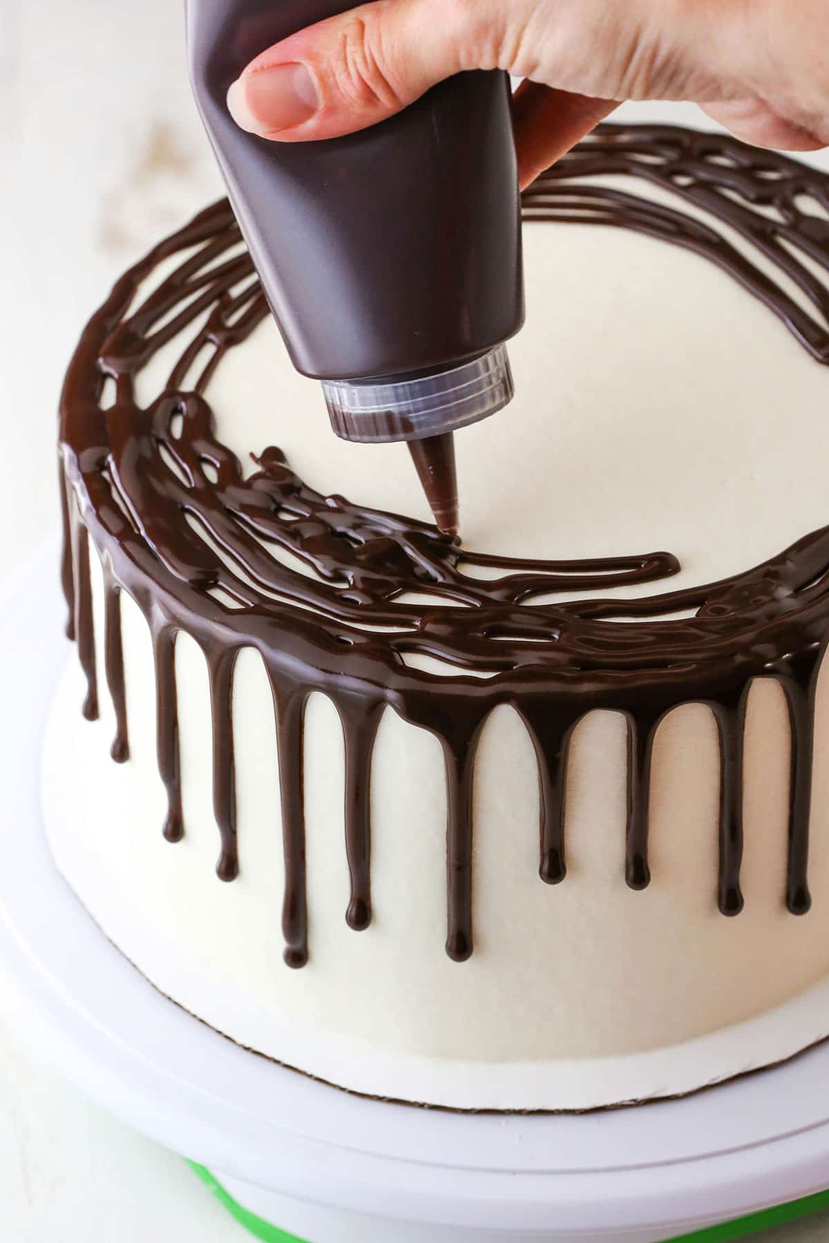 How to Make a Chocolate Drip Cake tutorial showing using a squeeze bottle to fill and cover the top of the cake with chocolate ganache