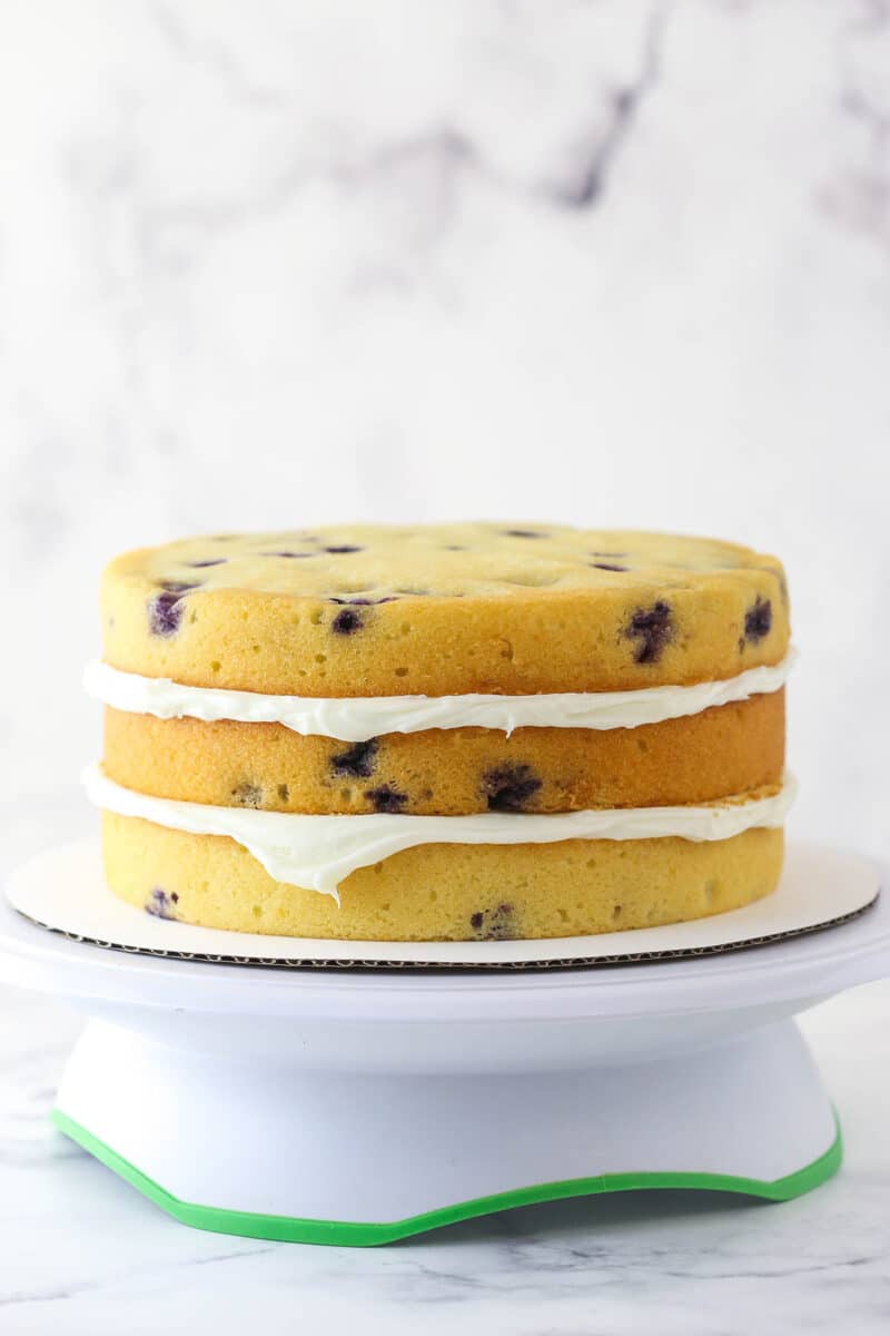 Stacking and filling layers of lemon blueberry cake with cream cheese frosting.