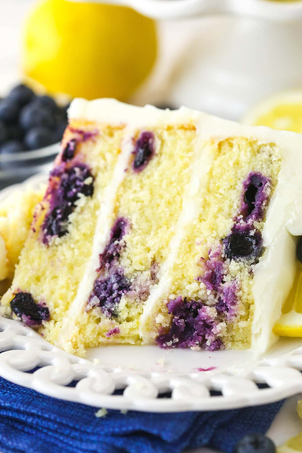 A slice of lemon blueberry cake on a plate with a bite taken out of it.