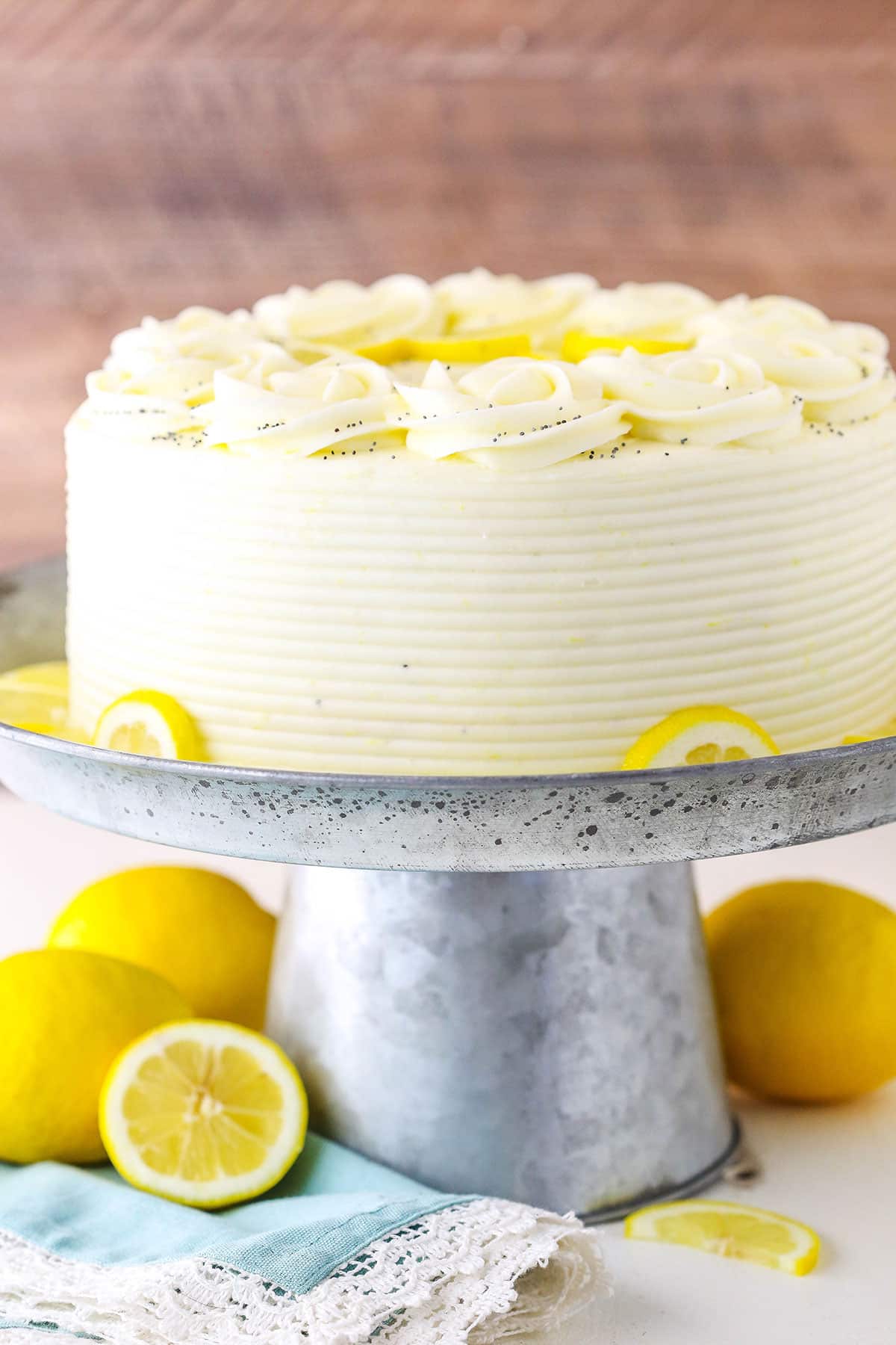 A full Lemon Poppyseed Cake on a gray cake stand on a white table