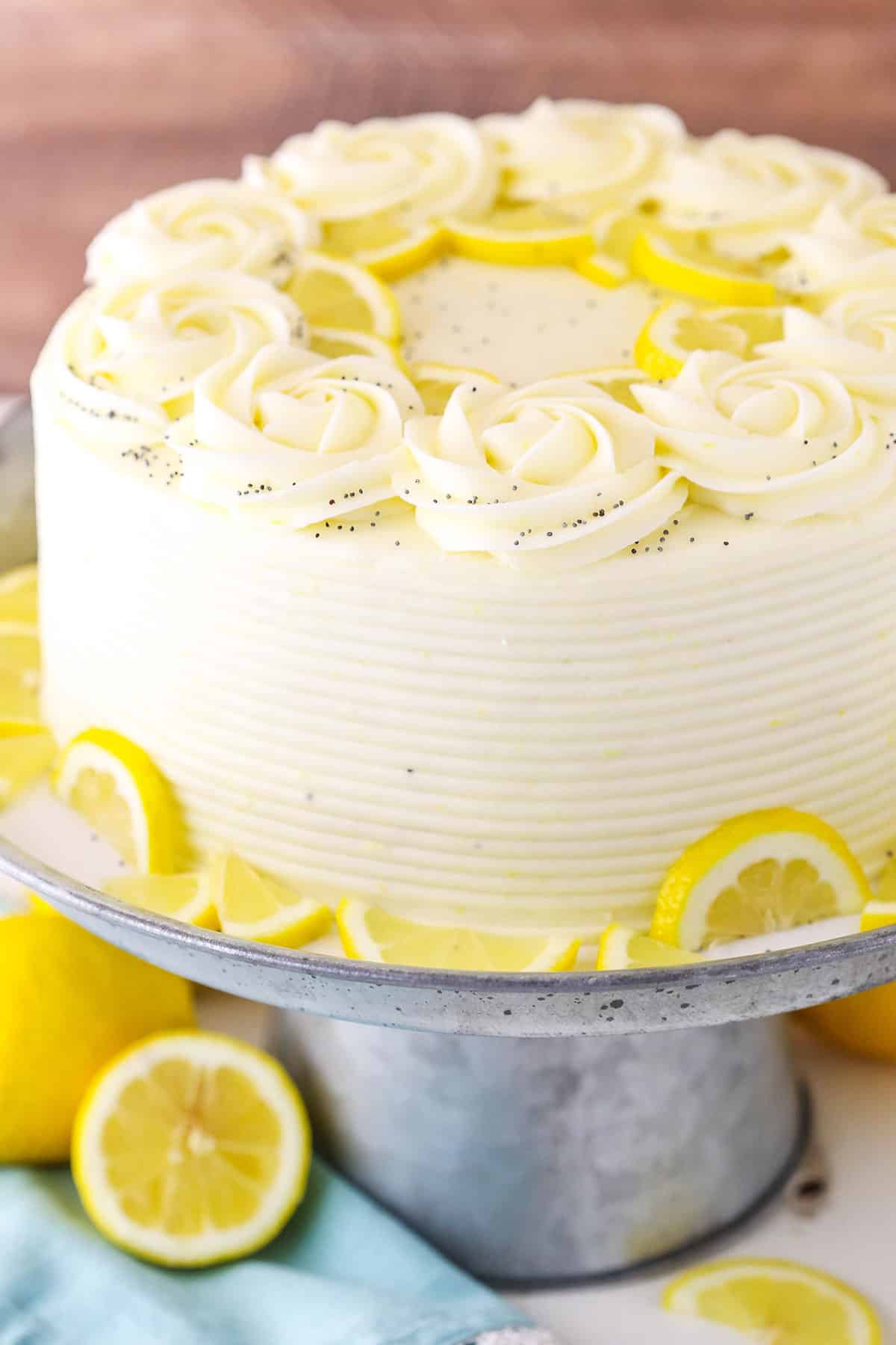 A full Lemon Poppyseed Cake on a gray cake stand on a white table