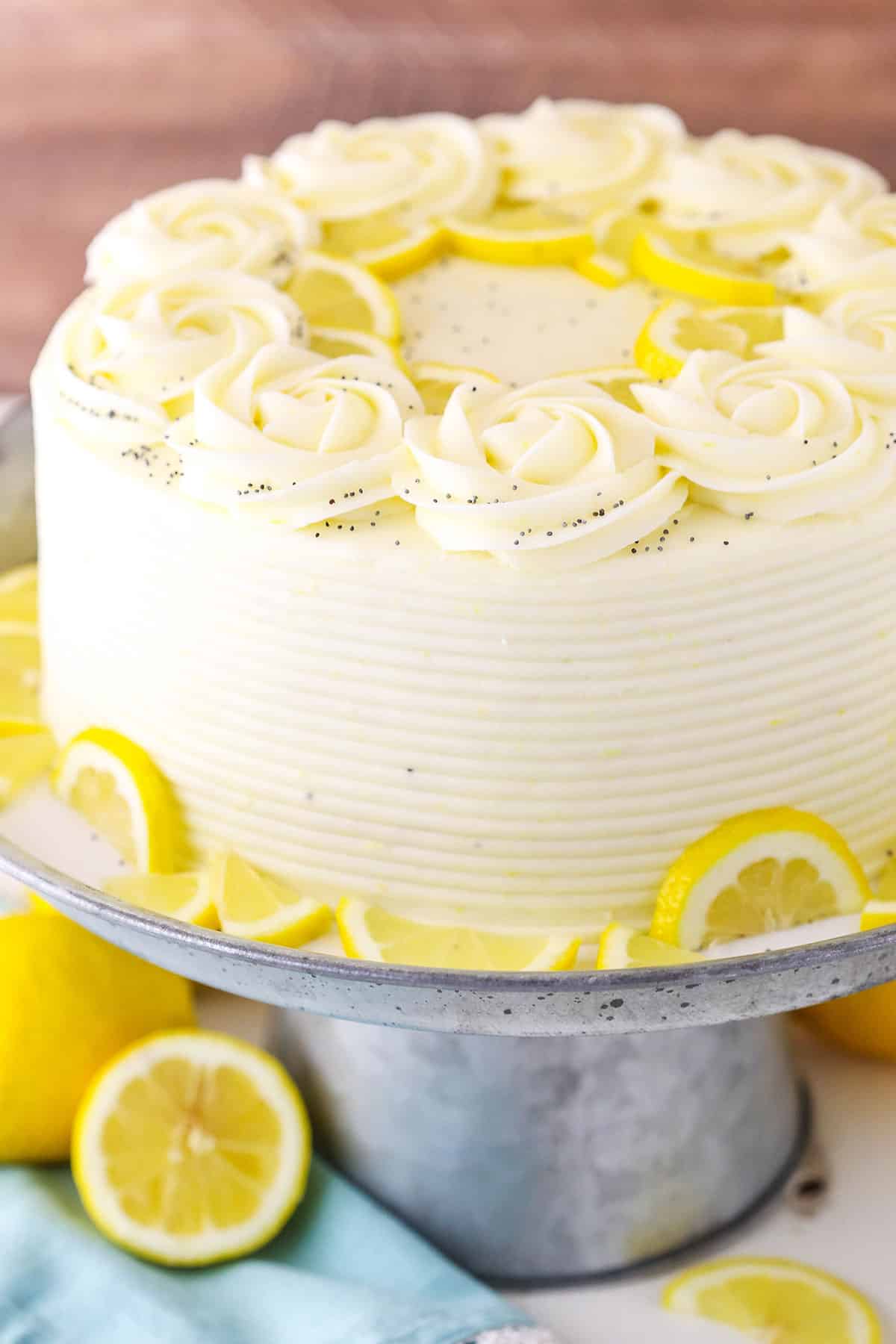This Lemon Poppyseed Cake is a tender, moist cake that's full of lemon flavor and poppy seeds! It's covered in a light lemon cream cheese frosting for a cake that's perfect for lemon lovers! A full Lemon Poppyseed Cake on a gray cake stand on a white table