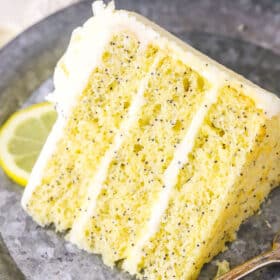 A slice of Lemon Poppyseed Cake next to a fork on a gray plate