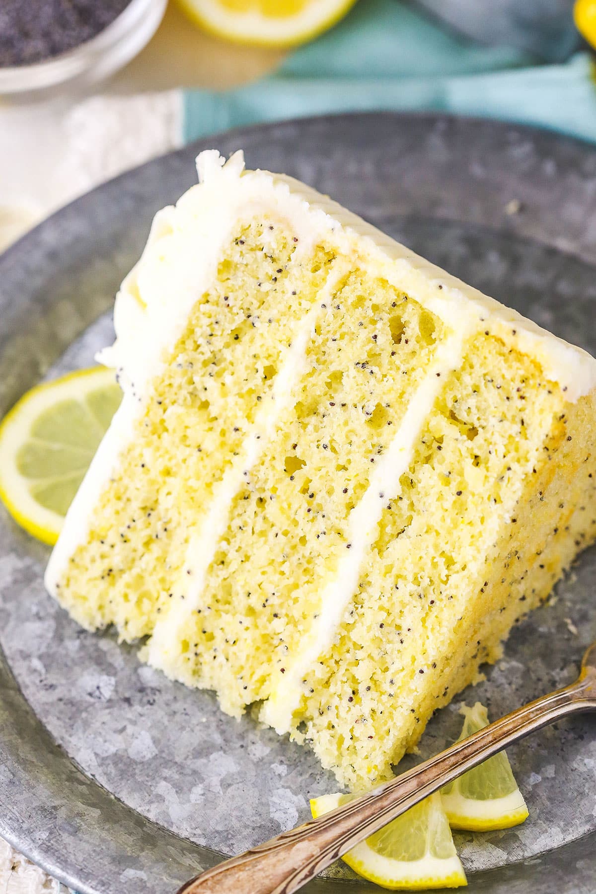 A slice of Lemon Poppyseed Cake next to a fork on a gray plate