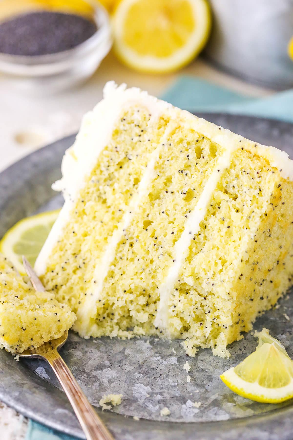 A slice of Lemon Poppyseed Cake with a bite removed next to a fork on a gray plate