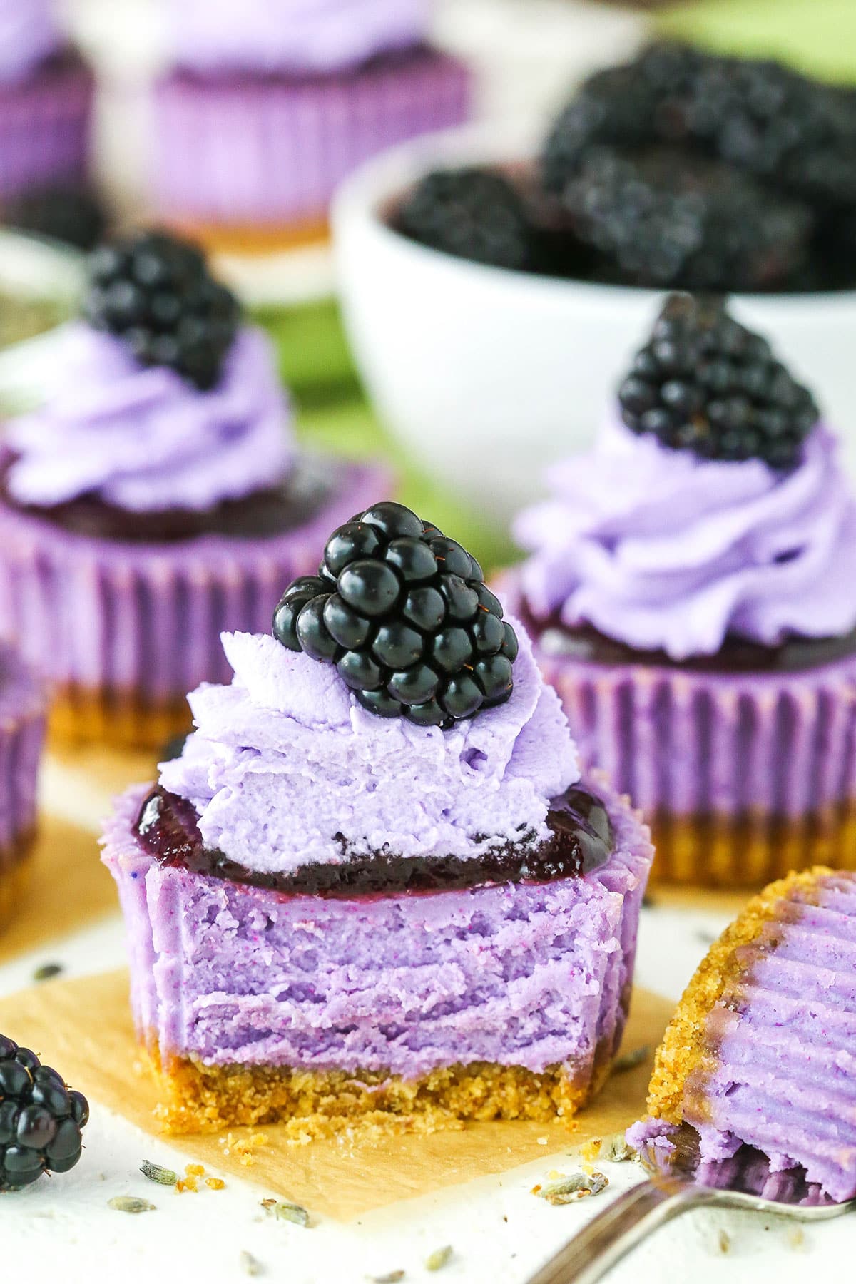 A Mini Blackberry Lavender Cheesecake with a bite taken out next to a fork on a white table top