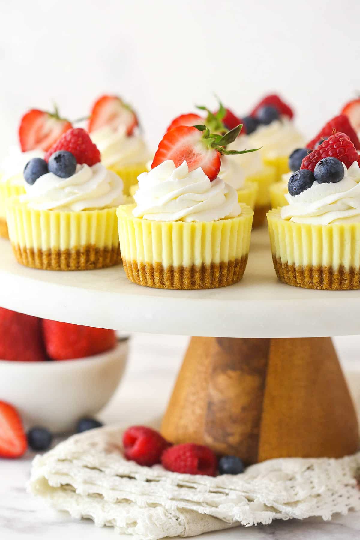 Mini cheesecakes on a cakes stand near a bowl of fresh berries.