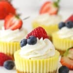 Mini cheesecakes on white surface surrounded by fresh berries.