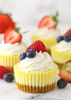 Mini cheesecakes on white surface surrounded by fresh berries.