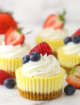 Mini cheesecakes on white surface surrounded by fresh berries.
