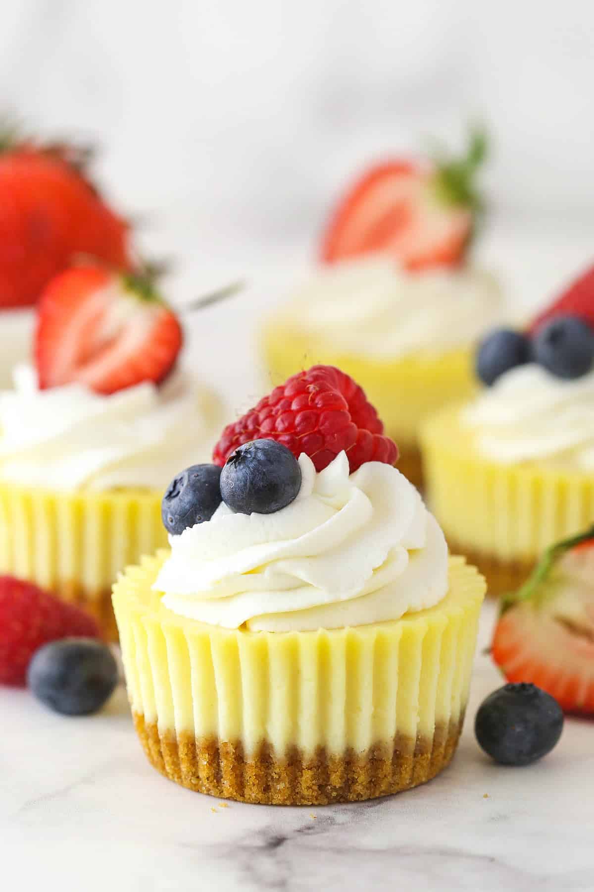 Mini cheesecakes on white surface surrounded by fresh berries.