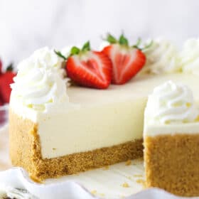 A whole no bake cheesecake on a serving platter with a slice taken out of it.