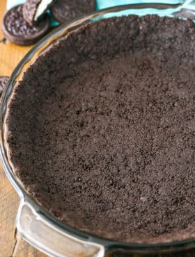 Oreo Cookie Crust in a clear glass pan on a wooden table