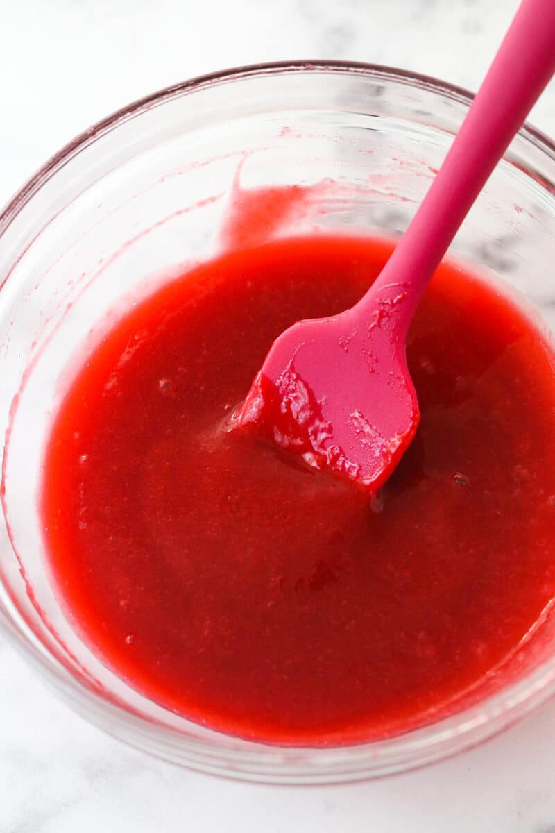 Raspberry filling with seeds removed cooling in a bowl with a rubber spatula.