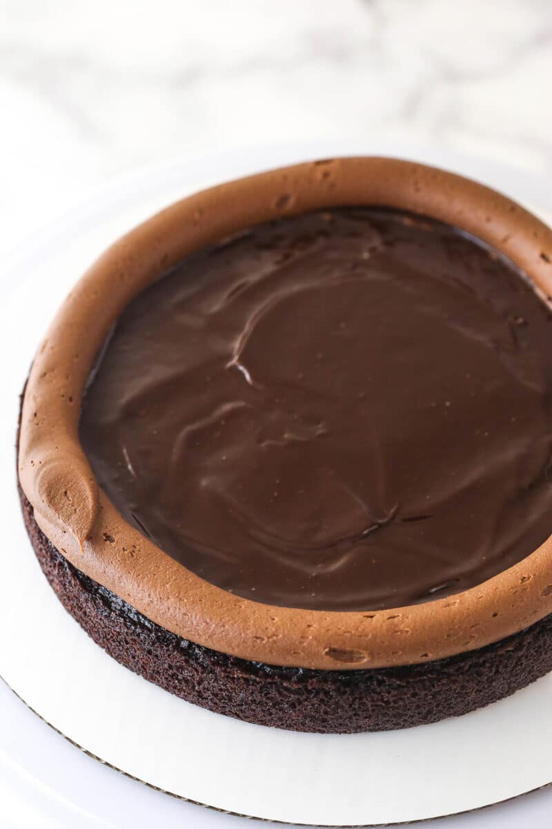 This chocolate raspberry cake is made of moist chocolate cake, smooth raspberry filling, dark chocolate frosting, and rich chocolate ganache. Spreading chocolate ganache in the center of a frosting dam on top of a layer of chocolate cake.