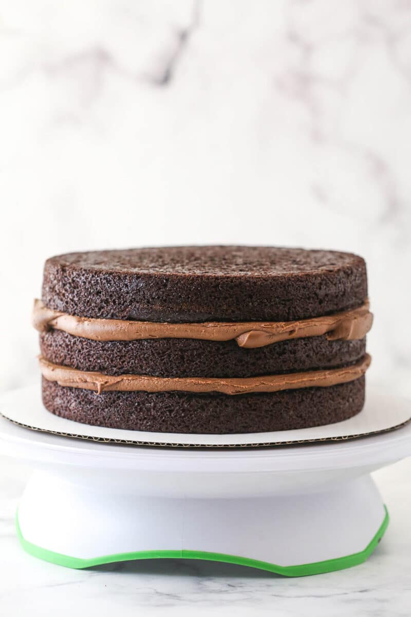 This chocolate raspberry cake is made of moist chocolate cake, smooth raspberry filling, dark chocolate frosting, and rich chocolate ganache. Placing the last chocolate cake layer on top of chocolate raspberry layer cake.