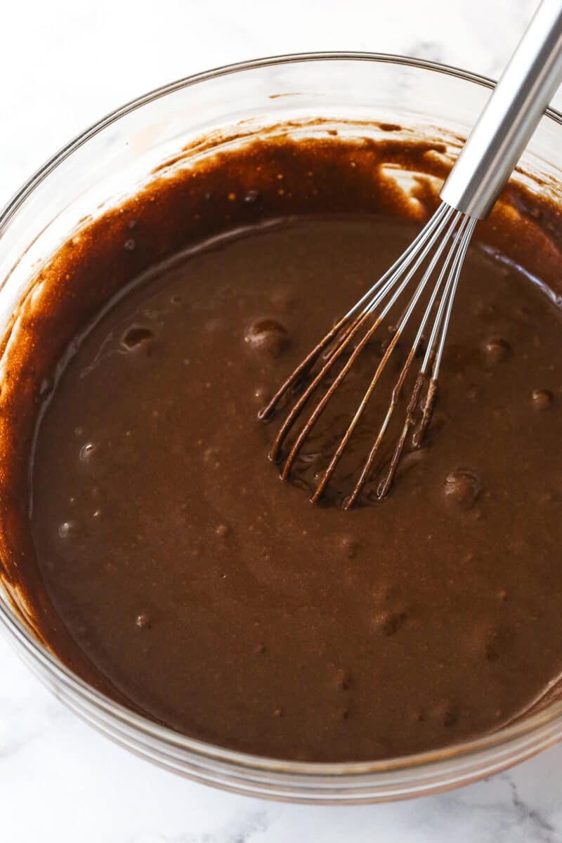 This chocolate raspberry cake is made of moist chocolate cake, smooth raspberry filling, dark chocolate frosting, and rich chocolate ganache. Mixing the wet ingredients into the dry ingredients for chocolate cake.