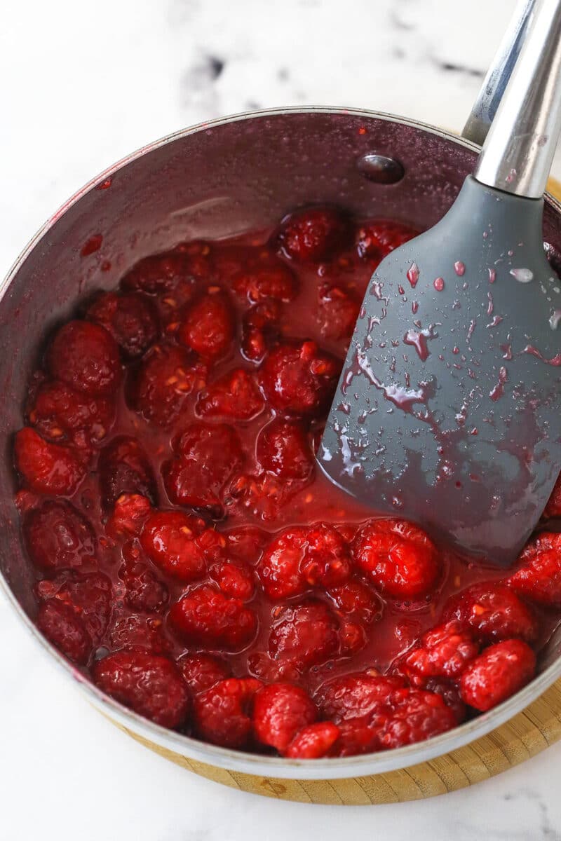 Coating raspberries in a mixture of melted sugar, water, and cornstarch in a pot and crushing them with a rubber spatula.