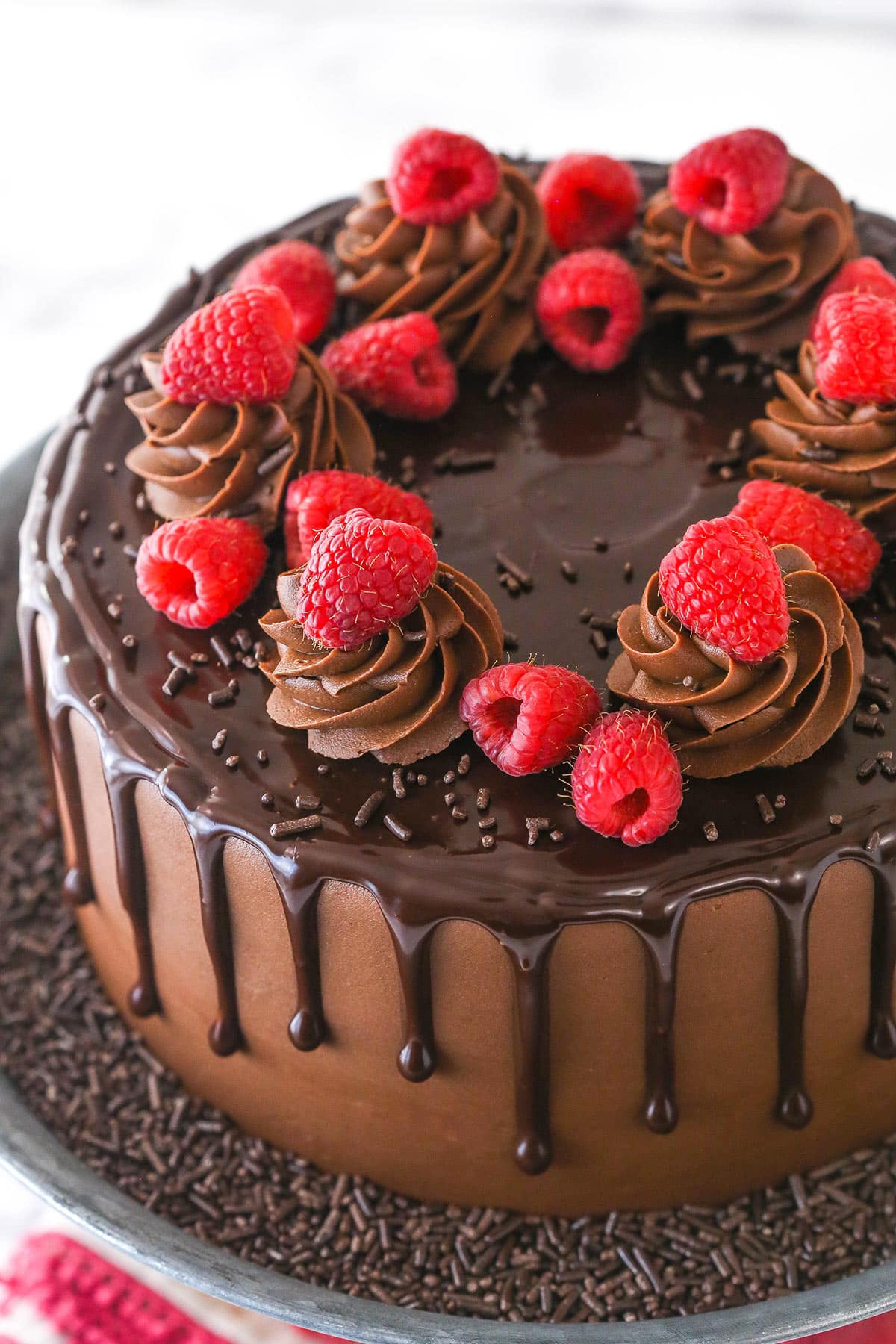 This chocolate raspberry cake is made of moist chocolate cake, smooth raspberry filling, dark chocolate frosting, and rich chocolate ganache. Overhead of a whole chocolate raspberry cake o n a cake platter.
