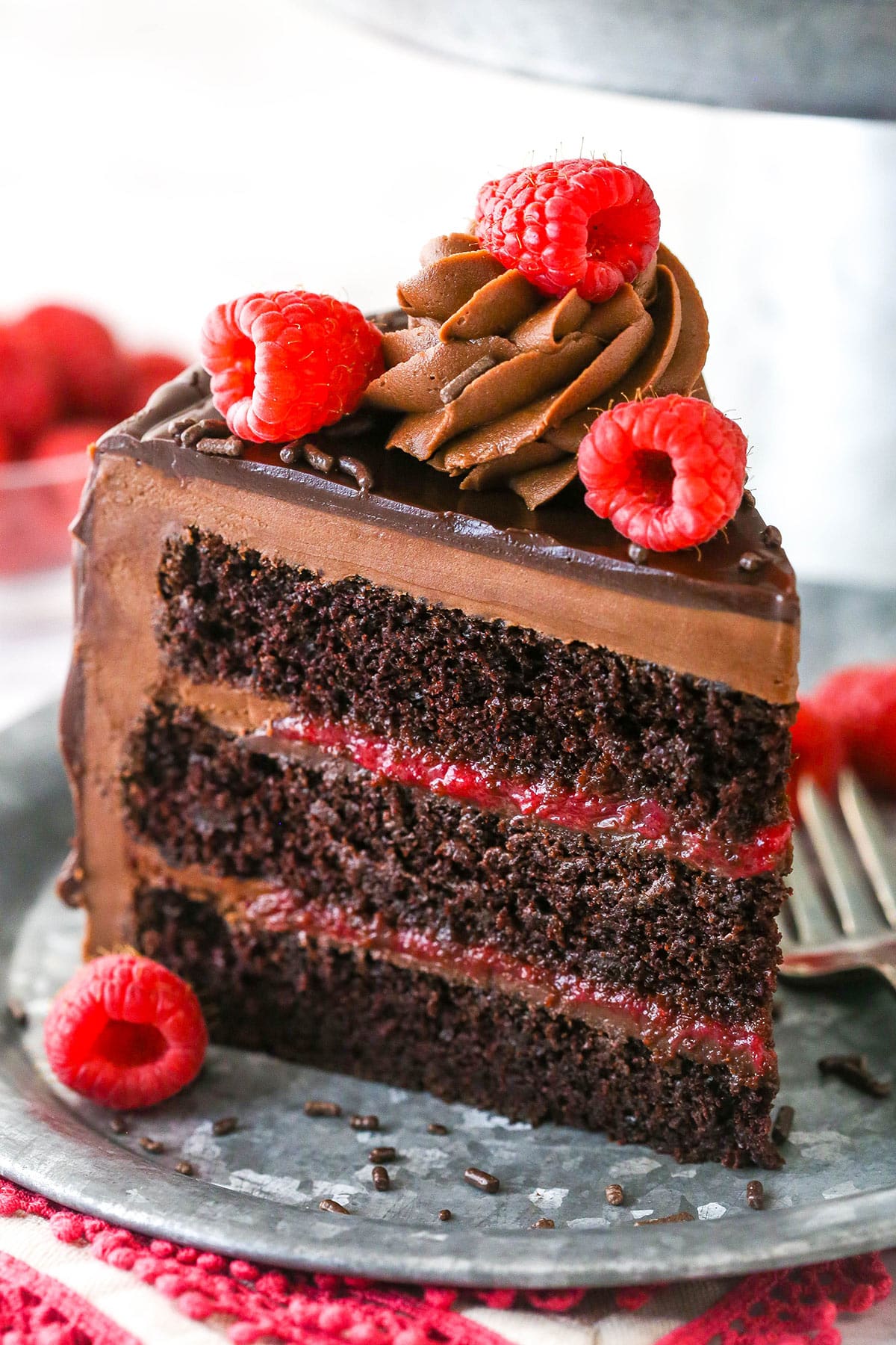 This chocolate raspberry cake is made of moist chocolate cake, smooth raspberry filling, dark chocolate frosting, and rich chocolate ganache. A slice of chocolate raspberry layer cake on a plate with a fork.
