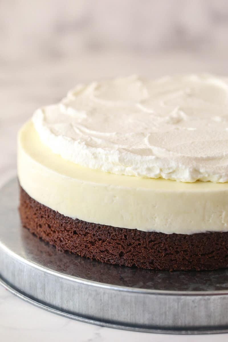 Spreading whipped cream over no-bake cheesecake filling on top of a brownie base.