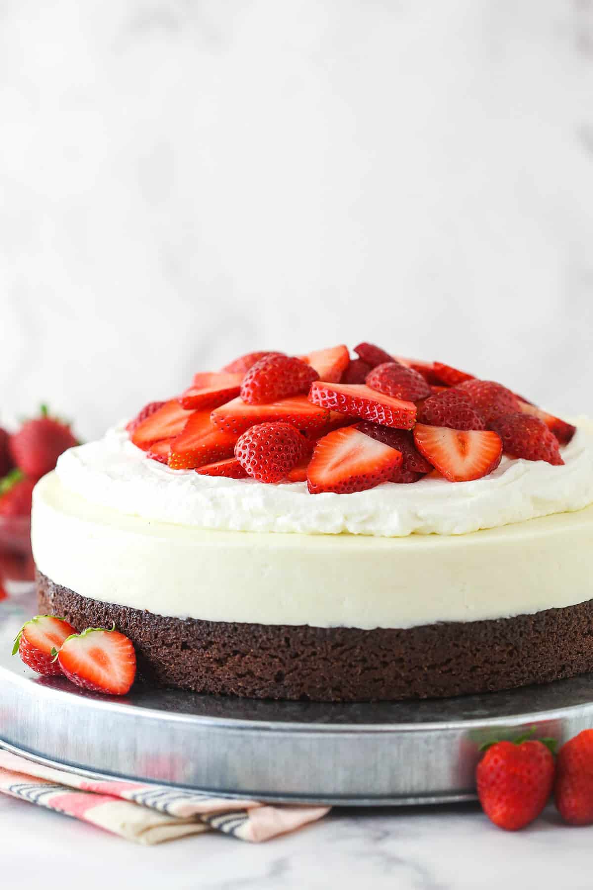 This brownie cheesecake is made up of a chewy brownie topped with no bake vanilla cheesecake, fresh whipped cream, and fresh strawberries. Strawberry brownie cheesecake on a serving platter.
