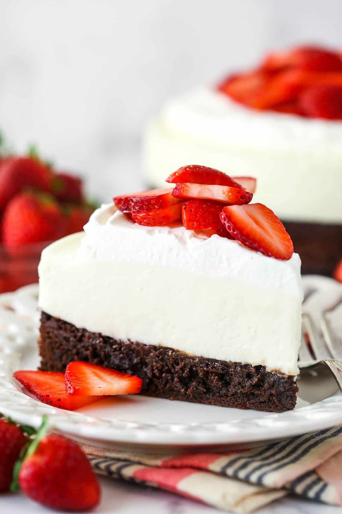 A slice of strawberry brownie cheesecake on a plate surrounded by fresh strawberries.