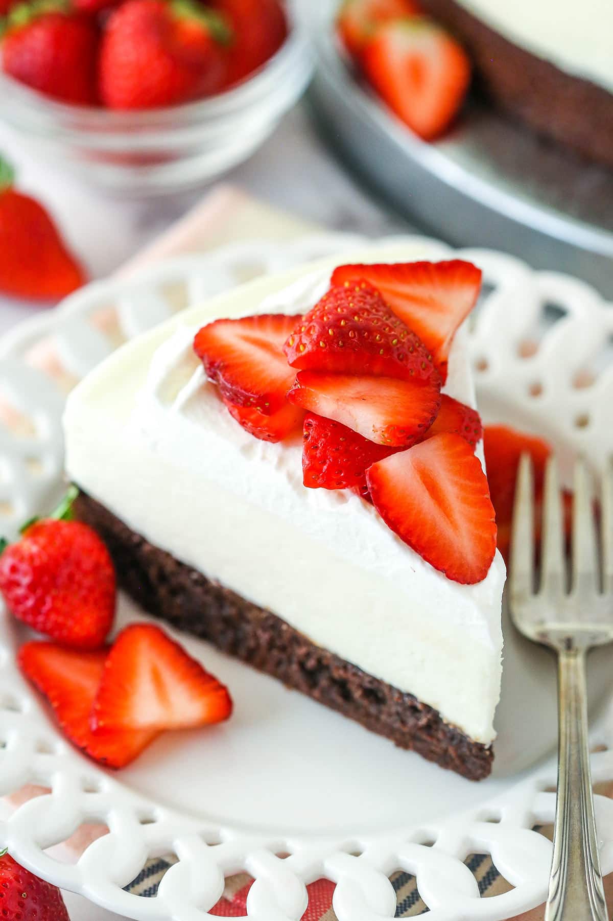 Overhead of a slice of strawberry brownie cheesecake on a plate surrounded by fresh strawberries.