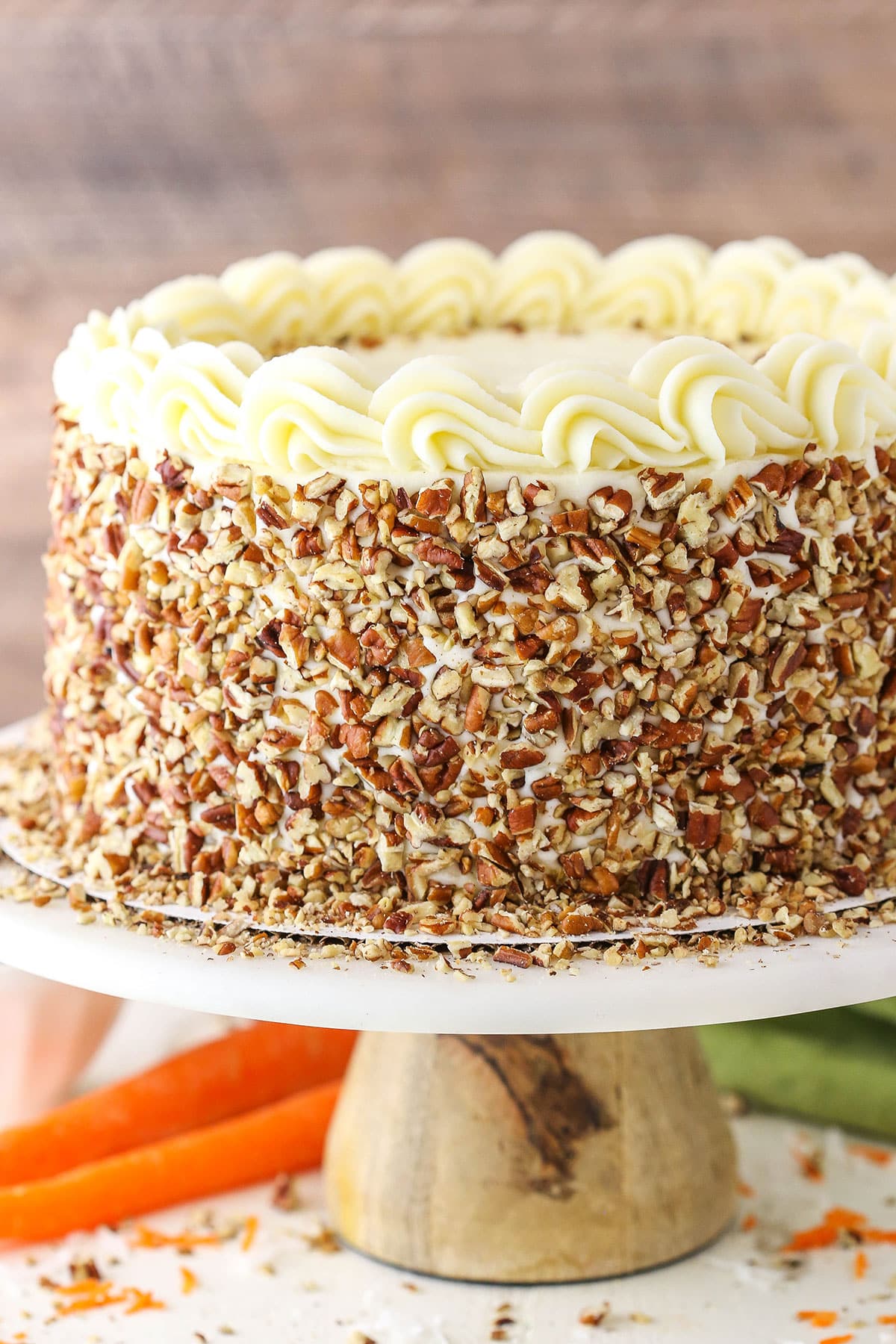 Side view of a full Carrot Cake on a white cake stand with a wooden base