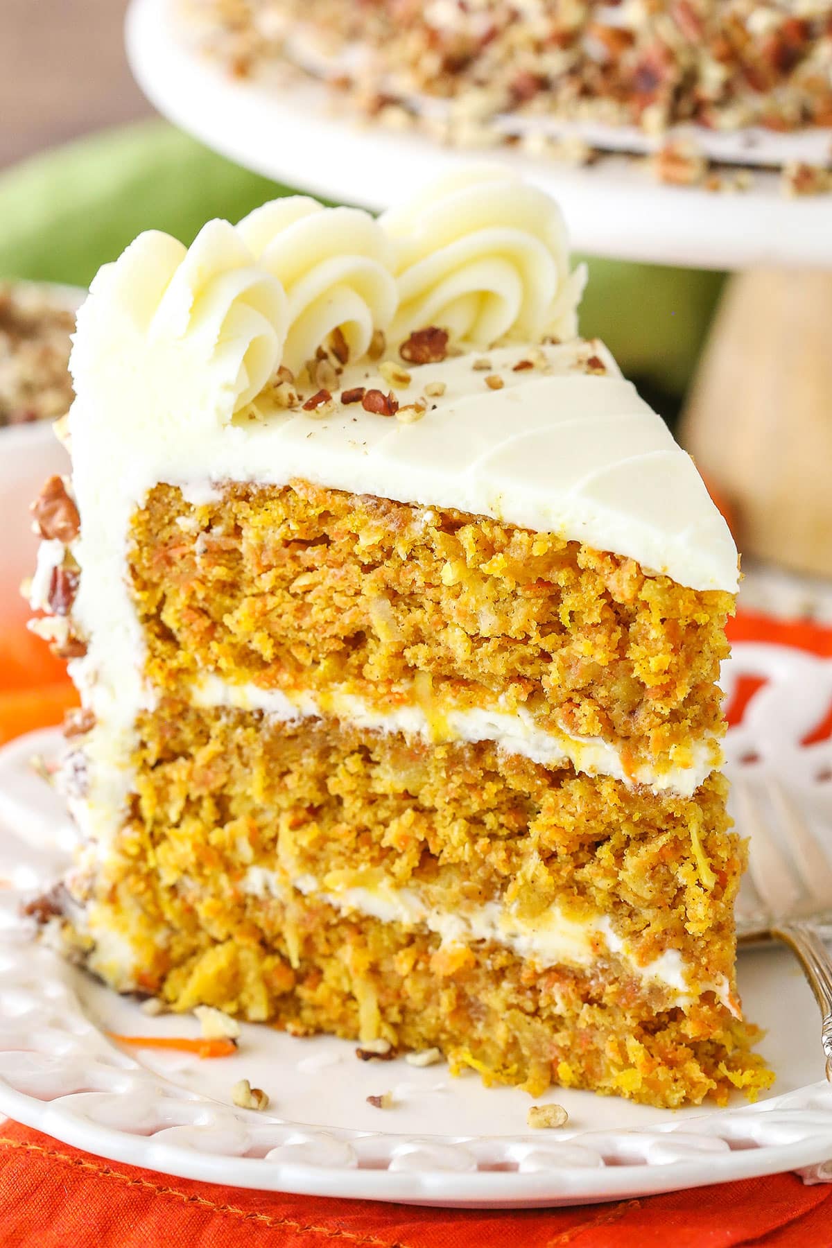 A slice of Carrot Cake next to a silver fork on a white plate